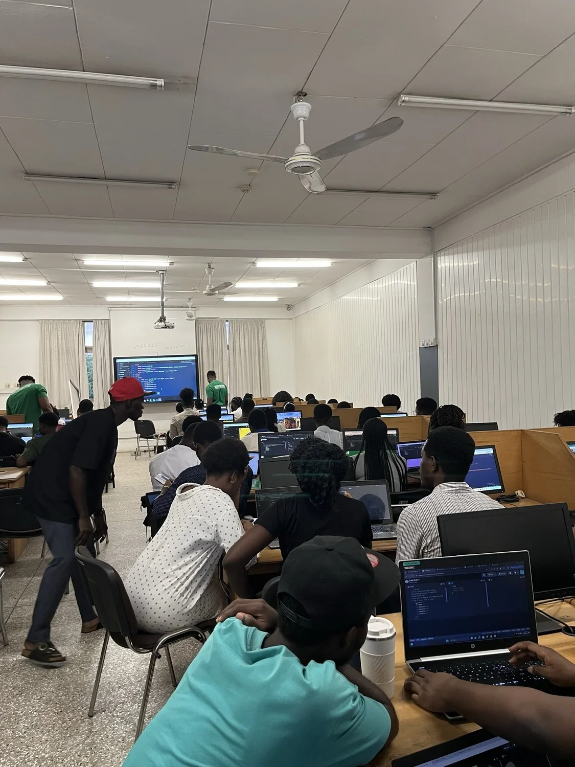 Participants working at rows of laptops across the lab while facilitators move between them.