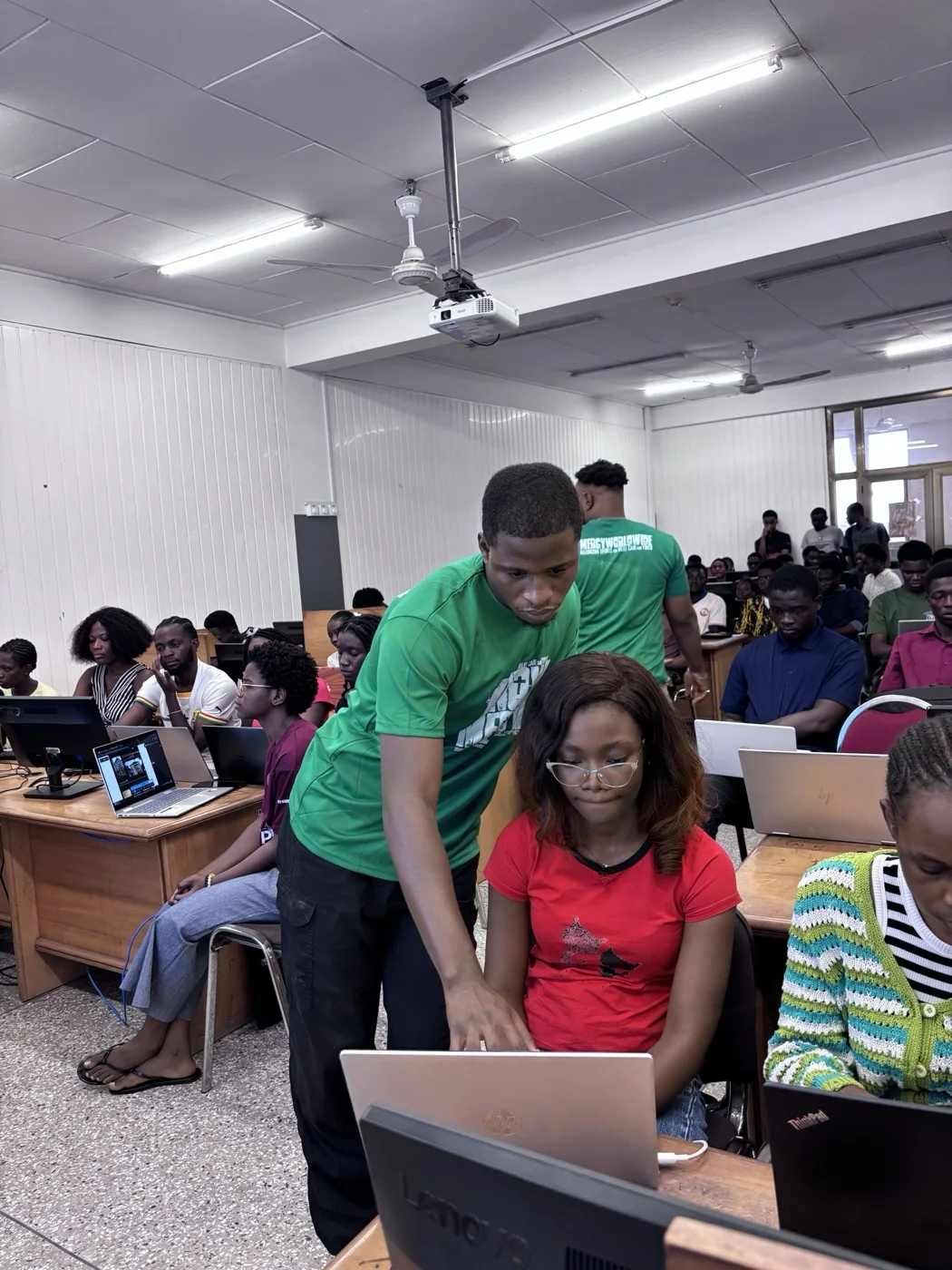 A volunteer leaning in to help a participant with something on her laptop during the session.