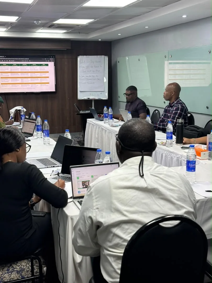 Participants working on laptops during a hands-on session, with notes on a flip chart behind them.